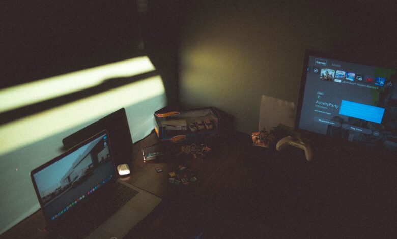 Dark room with a laptop and gaming console creating a moody tech atmosphere.