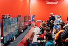 A lively group enjoys gaming at a Nintendo event in Zagreb, featuring multiple screens and vibrant atmosphere.