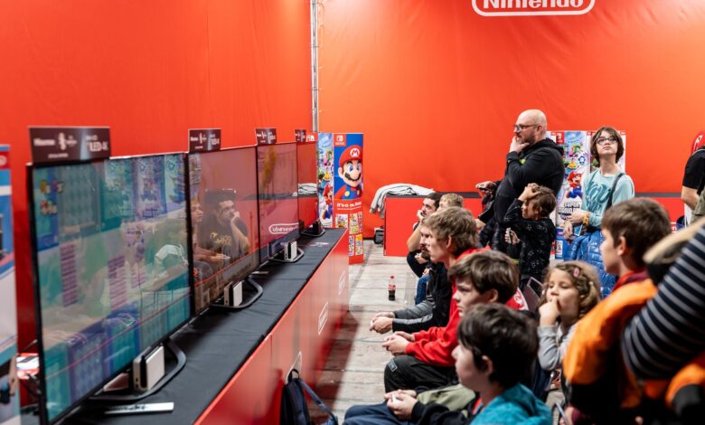 A lively group enjoys gaming at a Nintendo event in Zagreb, featuring multiple screens and vibrant atmosphere.