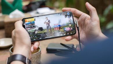 Person playing PUBG on smartphone outdoors with charging cable attached.