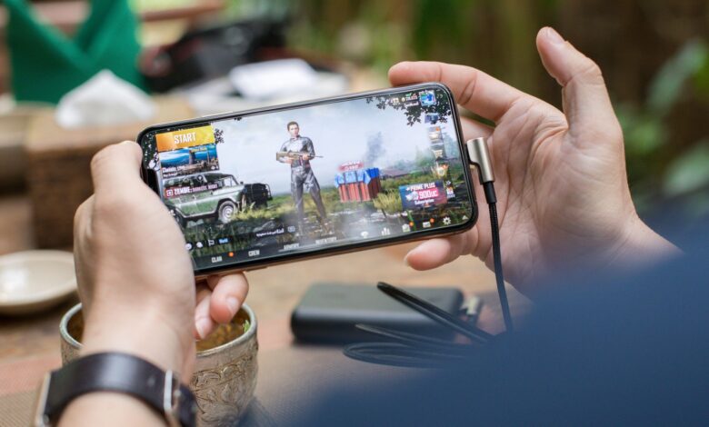Person playing PUBG on smartphone outdoors with charging cable attached.
