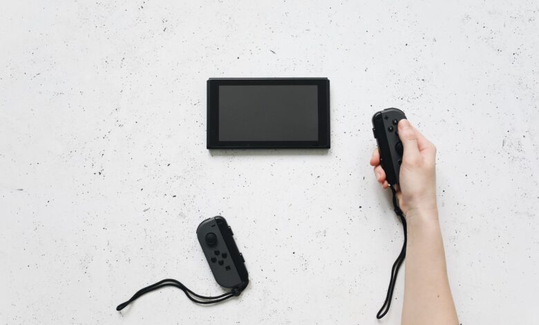 A person holds a Joy-Con controller with a Nintendo Switch on a white textured surface.