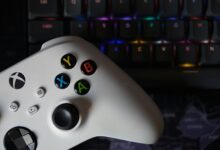 Game controller beside illuminated RGB keyboard, highlighting technology and gaming equipment.