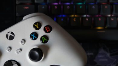Game controller beside illuminated RGB keyboard, highlighting technology and gaming equipment.