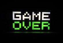Illuminated 'Game Over' sign in pixel art style with neon green and white colors on a dark background.
