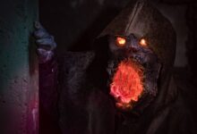 A menacing monster with glowing eyes and mouth in detailed horror cosplay peeking from a shadowy corner.