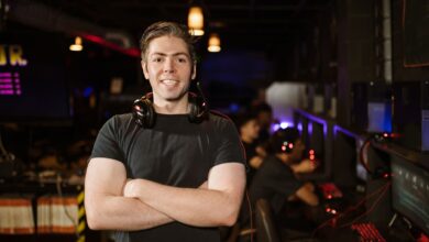 Smiling gamer standing with headphones in an illuminated gaming arena.