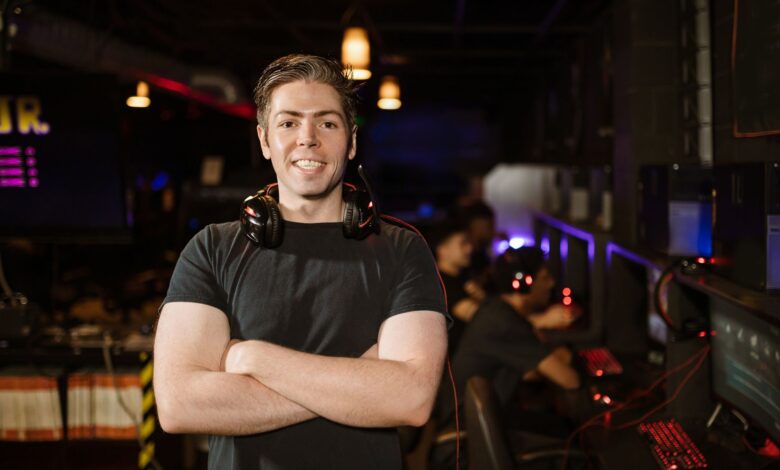 Smiling gamer standing with headphones in an illuminated gaming arena.