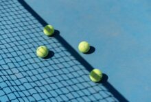 Four tennis balls resting on a blue tennis court with shadows from a net.