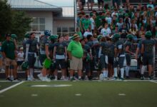 High school football players and coach on sidelines during a game.