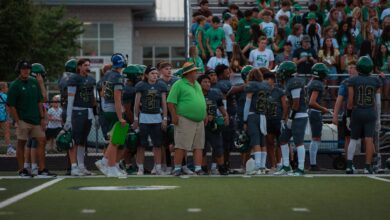 High school football players and coach on sidelines during a game.