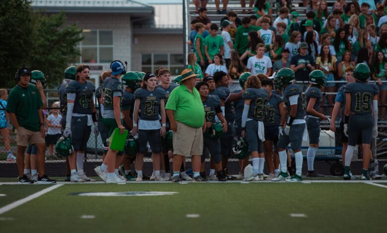 High school football players and coach on sidelines during a game.