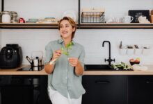 Smiling woman with vegetables in a stylish kitchen showcasing modern interior design.