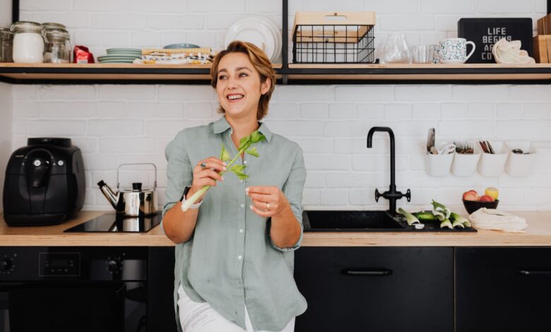Smiling woman with vegetables in a stylish kitchen showcasing modern interior design.