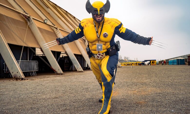 A cosplayer vividly dressed as Wolverine with claws extended outdoors showing excitement.