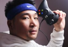 Asian man in white sweatshirt holding a gaming controller, focused on gaming.