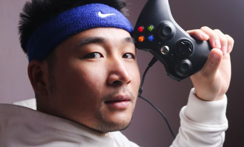 Asian man in white sweatshirt holding a gaming controller, focused on gaming.