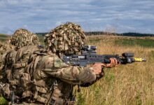 Military soldiers in camouflage gear practicing combat in a grassy countryside.
