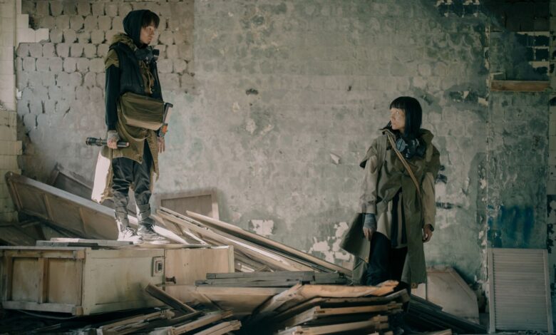 Two people exploring a desolate, abandoned building in post-apocalyptic attire.