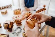 Close-up of hands engaging with wooden brain teasers on a table indoors.