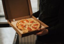 A person holds an open box with a freshly baked pizza topped with tomatoes and cheese.