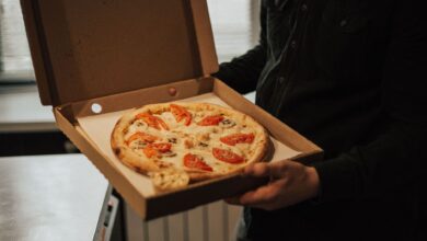 A person holds an open box with a freshly baked pizza topped with tomatoes and cheese.