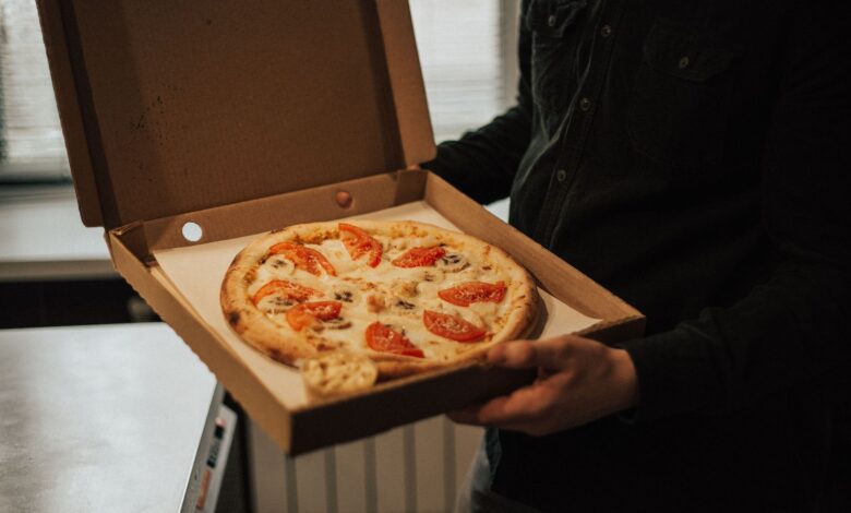 A person holds an open box with a freshly baked pizza topped with tomatoes and cheese.