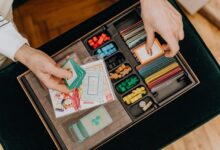 Close-up of hands holding cards in a colorful board game setup, showcasing strategy play.