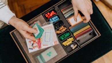 Close-up of hands holding cards in a colorful board game setup, showcasing strategy play.