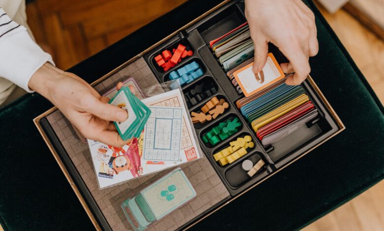 Close-up of hands holding cards in a colorful board game setup, showcasing strategy play.