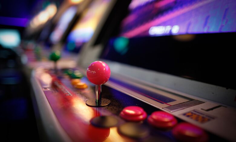 Close-up of a colorful vintage arcade machine with glowing joysticks and buttons in a dimly lit game room.