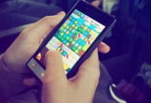 Hands holding a smartphone with a colorful puzzle game on the screen, displaying modern technology.