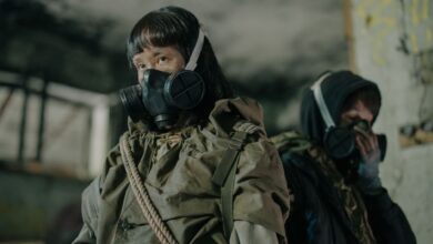 Man and woman in gas masks amidst a dystopian post-apocalyptic urban setting.