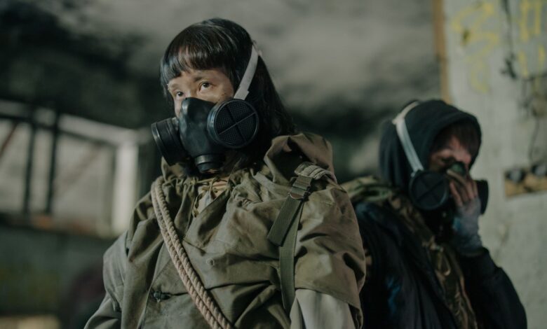 Man and woman in gas masks amidst a dystopian post-apocalyptic urban setting.