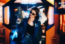 Fashionable young woman in an arcade holding a toy gun enjoying leisure time.
