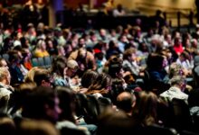 A diverse crowd seated in an auditorium, engaged in an indoor event.