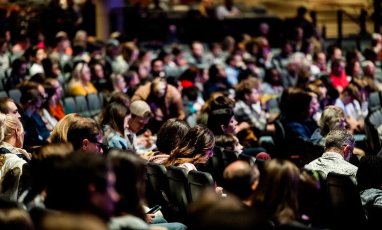 A diverse crowd seated in an auditorium, engaged in an indoor event.