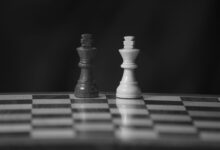 Close-up black and white photo of chess king pieces on a board against a dark background.