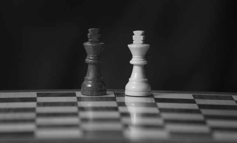 Close-up black and white photo of chess king pieces on a board against a dark background.