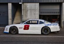 White race car parked outdoors near a garage on a sunny day.