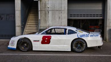 White race car parked outdoors near a garage on a sunny day.