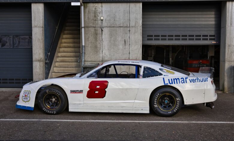 White race car parked outdoors near a garage on a sunny day.
