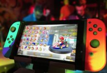 Close-up of a Nintendo Switch showing Mario Kart selection screen, gaming atmosphere in the background.