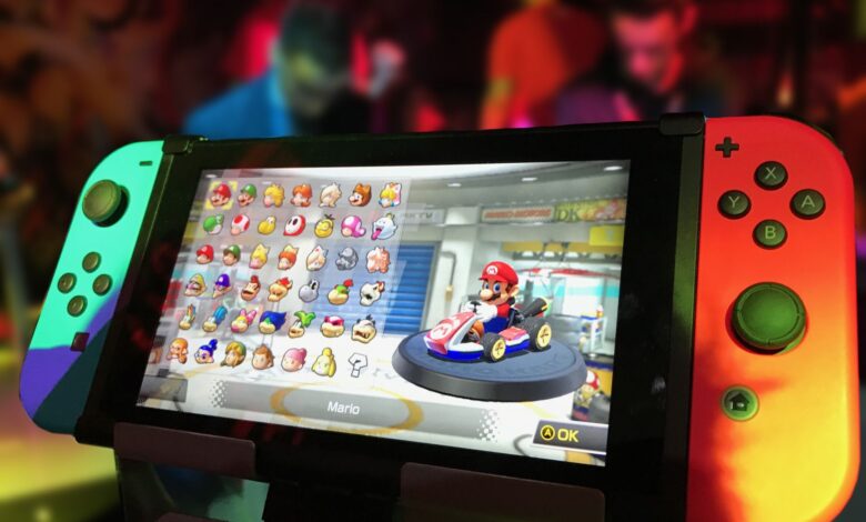 Close-up of a Nintendo Switch showing Mario Kart selection screen, gaming atmosphere in the background.