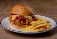Close-up of a crispy fried chicken burger with melted cheese and fries on a plate.