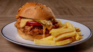 Close-up of a crispy fried chicken burger with melted cheese and fries on a plate.