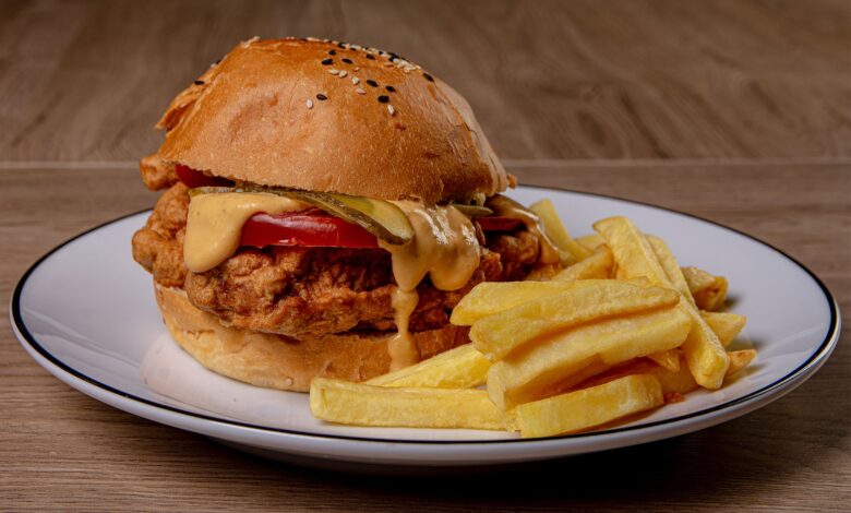 Close-up of a crispy fried chicken burger with melted cheese and fries on a plate.
