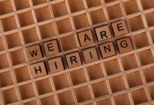 Wooden letter tiles arranged to spell 'We Are Hiring' on a wooden grid background.