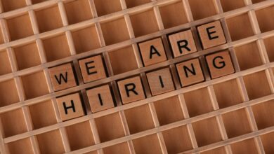 Wooden letter tiles arranged to spell 'We Are Hiring' on a wooden grid background.
