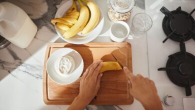 Person slicing banana on wooden board with cereals and milk for a healthy breakfast.